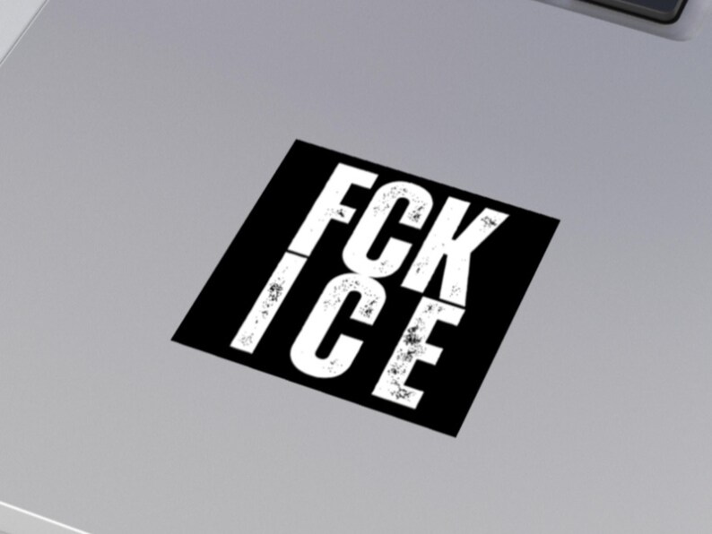 May include: A black square sticker with the white text "FCK ICE" in a distressed font. The sticker is angled on a light grey surface.