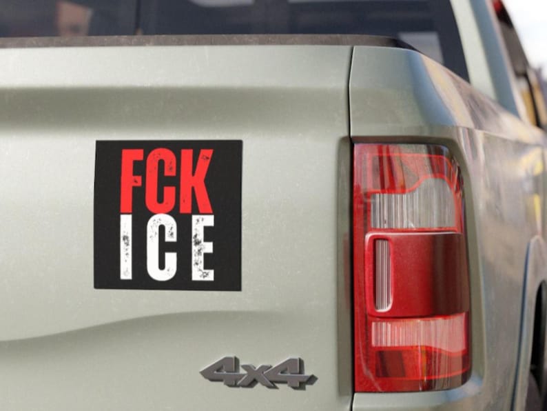 May include: A black and red sticker with the words "FCK ICE" in white lettering is attached to the rear of a light-coloured vehicle. The vehicle's taillight is visible on the right, and the 4x4 emblem is below the sticker.