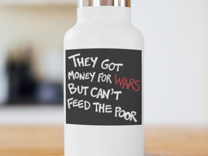 May include: White water bottle with a silver lid. The bottle has a black rectangle with white text that reads "They Got Money For Wars But Can't Feed The Poor". The word "Wars" is in red.