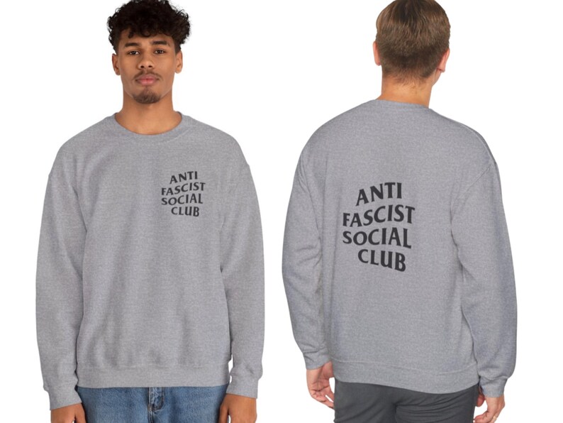 K&ouml;nnte beinhalten: Ein hellgraues Sweatshirt mit dem schwarzen Aufdruck "ANTI FASCIST SOCIAL CLUB" auf der Vorder- und R&uuml;ckseite. Das Sweatshirt hat einen Rundhalsausschnitt.