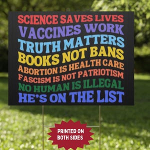 Op de afbeelding: Zwart bord met kleurrijke tekst: "WETENSCHAP REDT LEVENS, VACCINS WERKEN, WAARHEID DOET ERTOE, BOEKEN GEEN VERBODEN, ABORTUS IS GEZONDHEIDSZORG, FASCISME IS GEEN PATRIOTISME, GEEN MENS IS ILLEGAAL, HIJ STAAT OP DE LIJST". Bedrukt aan beide zijden.