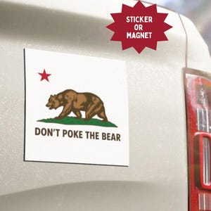 May include: A white sticker or magnet featuring the California state flag design. The design includes a brown bear, a red star, green grass, and the text "DON'T POKE THE BEAR". The sticker is affixed to the back of a vehicle.