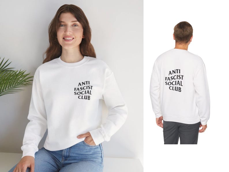 K&ouml;nnte beinhalten: Wei&szlig;es Sweatshirt mit dem Text "ANTI FASCIST SOCIAL CLUB" in Schwarz auf der Vorder- und R&uuml;ckseite. Das lang&auml;rmlige Sweatshirt hat einen Rundhalsausschnitt. Die Person auf dem Bild tr&auml;gt eine blaue Jeans.
