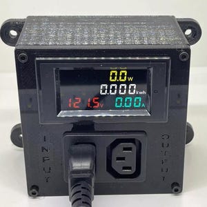 May include: Black electrical device with a digital display showing voltage, wattage, and amperage readings. The device has an input and output port, and a power cord is plugged into the front. The display shows 0.0W, 0.000kWh, 121.5V, and 0.00A.