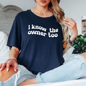May include: A navy blue t-shirt with the text "i know the owner too" in white, retro-style lettering.