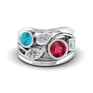 May include: A silver ring with a unique design, featuring a round, bright blue gemstone and a round, deep red gemstone. The ring also includes several smaller, clear gemstones and leaf-shaped accents.