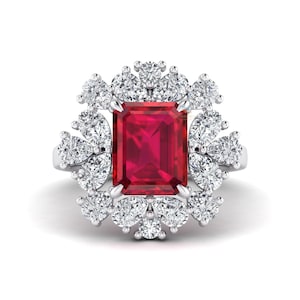 May include: A silver ring featuring a large, rectangular, deep red gemstone at the center, surrounded by a halo of smaller, round, clear gemstones. The ring's design is symmetrical and elegant, with the gemstones set in a floral-like pattern.