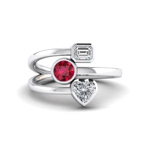 May include: A silver ring with three gemstones: a round ruby, an emerald-cut diamond, and a heart-shaped diamond. The ring's band wraps around the finger, creating a unique and elegant design. The gemstones are set in a prong setting.