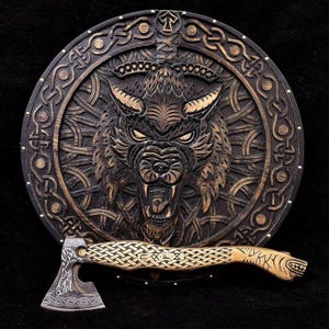 Könnte beinhalten: Ein Holzschild mit einem geschnitzten Wolfskopf und einem komplizierten keltischen Knotenmuster. Der Schild ist mit goldenen Akzenten verziert und hat eine kleine Axt mit einem geflochtenen Griff.