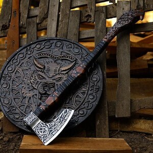 May include: A black and brown axe with a carved wooden handle and a shield with a wolf design. The axe blade is engraved with the text "CONQUERED WOLF NEVERLY FEARLESS FOREVER".