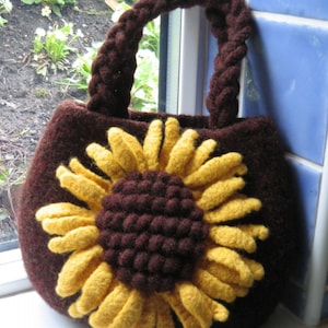 May include: A brown crocheted handbag with a large sunflower design. The sunflower is made of yellow yarn and has a brown center.
