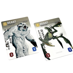 May include: Two rectangular game cards labeled Beast Token Unit. The left card features a white, furry, bipedal creature. The right card displays a green, multi-limbed, insectoid creature. Both cards include numerical values in red and blue icons.