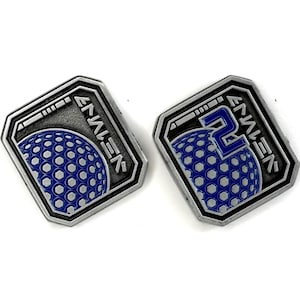 May include: Two silver-colored metal pins with a blue and white design. One pin features a blue sphere with a pattern, and the other has a blue number 2. Both pins have the word "ENALEN" in white text.