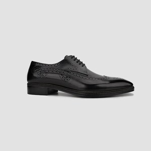 Puede incluir: Un zapato de vestir negro de cuero con dise&ntilde;o de ala. El zapato presenta perforaciones decorativas y una suela cosida. Los cordones son negros y el zapato tiene un tac&oacute;n bajo. El zapato est&aacute; sobre un fondo neutro.