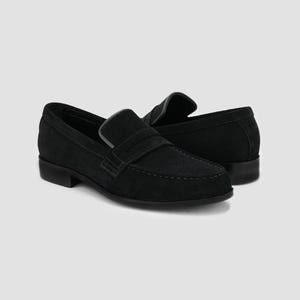May include: A pair of black suede penny loafers. The shoes have a classic design with a rounded toe, a strap across the vamp, and a low heel. The stitching is visible, and the shoes are set against a neutral background.