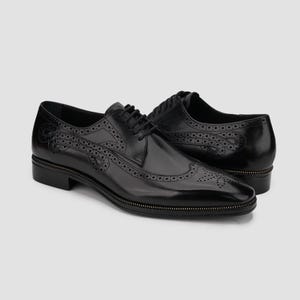 Puede incluir: Par de zapatos de vestir de cuero negro con intrincados detalles brogue y un ribete con cremallera en la suela. Los zapatos presentan un dise&ntilde;o cl&aacute;sico con cordones y un acabado pulido, adecuados para ocasiones formales. Miden unos 28 cm.