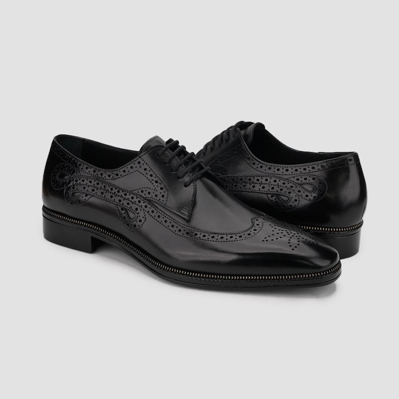 Puede incluir: Par de zapatos de vestir de cuero negro con intrincados detalles brogue y un ribete con cremallera en la suela. Los zapatos presentan un dise&ntilde;o cl&aacute;sico con cordones y un acabado pulido, adecuados para ocasiones formales. Miden unos 28 cm.