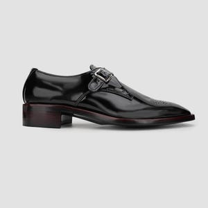 May include: A black leather dress shoe with a buckle closure. The shoe has a low heel and a pointed toe with decorative perforations. The sole has a dark red trim.