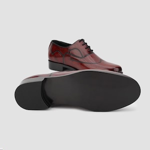 May include: A pair of burgundy leather dress shoes with black laces and stitching. One shoe is upright, and the other is positioned to show the sole. The shoes have a glossy finish and a classic wingtip design.