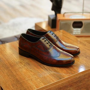 May include: A pair of brown leather dress shoes with black laces, displayed on a wooden surface. The shoes have a glossy finish and a classic wingtip design. A vintage radio is visible in the background, suggesting a classic or retro theme.