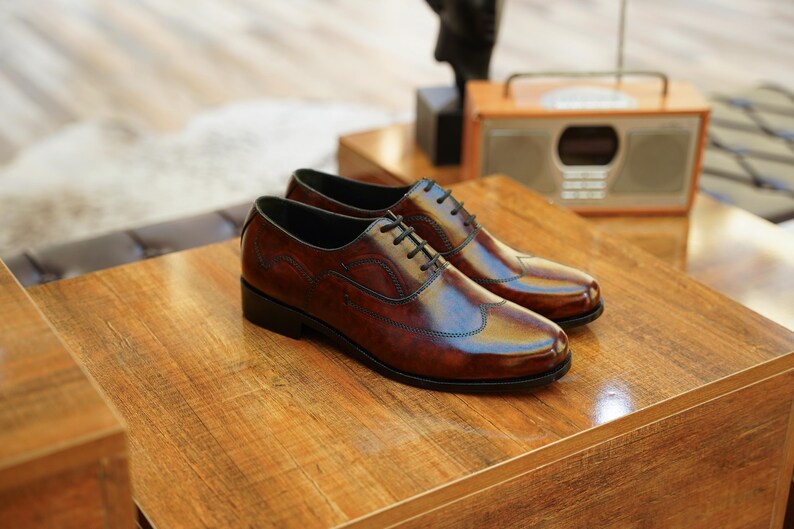 May include: A pair of brown leather dress shoes with black laces, displayed on a wooden surface. The shoes have a glossy finish and a classic wingtip design. A vintage radio is visible in the background, suggesting a classic or retro theme.
