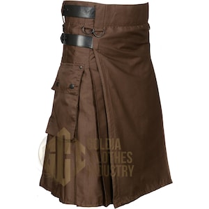 May include: A brown utility kilt featuring two black leather straps with metal buckles at the waist, two metal D-rings, and a large cargo pocket on the side with snap button closures. The garment has a pleated design and a smooth fabric finish.