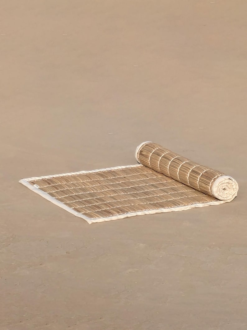 Puede incluir: Una esterilla de bamb&uacute; rectangular enrollada con un borde blanco. La esterilla est&aacute; parcialmente desenrollada, revelando un patr&oacute;n tejido de finas tiras de bamb&uacute; marr&oacute;n claro. La secci&oacute;n enrollada muestra el mismo material de bamb&uacute;.
