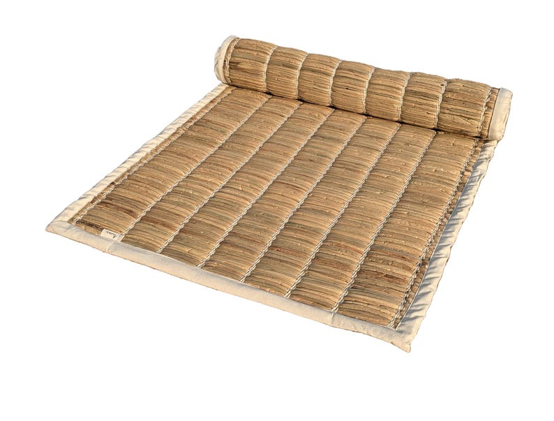 Puede incluir: Una esterilla rectangular enrollada, hecha de fibras naturales tejidas. La esterilla es principalmente beige con un borde beige claro y una secci&oacute;n enrollada en la parte superior. La textura tejida es visible, y la esterilla parece dise&ntilde;ada para la comodidad y la relajaci&oacute;n.