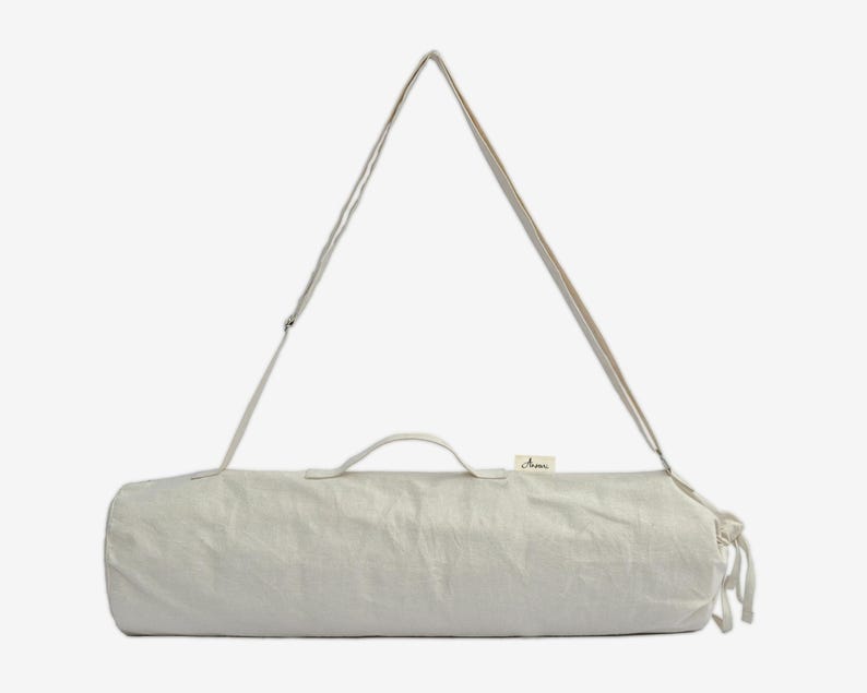 Puede incluir: Una bolsa de esterilla de yoga de color beige claro con una correa para el hombro y un asa. La bolsa cil&iacute;ndrica est&aacute; hecha de una tela texturizada y tiene una peque&ntilde;a etiqueta cerca del asa. La correa es ajustable y la bolsa tiene un cierre de cord&oacute;n.
