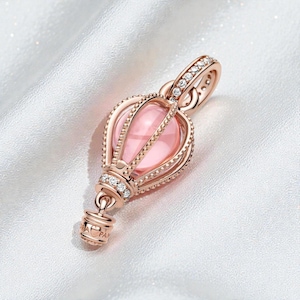 Può includere: Ciondolo in oro rosa a forma di mongolfiera con una gemma rosa al centro. Il ciondolo è adornato con piccole pietre chiare scintillanti e dettagli intricati. Include un'asola per una collana.