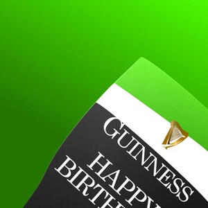 May include: A tilted Guinness Happy Birthday glass against a green background. The glass has a black section with white text and a gold harp logo. A text box at the top says, "The glass tilts to the right as it gets drunk."
