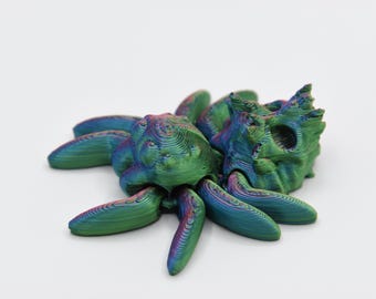 May include: A 3D-printed sculpture of a creature, with a layered design in green, blue, and purple. The sculpture has multiple legs and a textured body. The artwork is set against a white background. The sculpture could be an insect or arachnid.