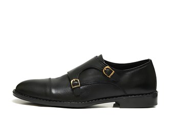 May include: Black leather dress shoe with a double monk strap design. The shoe features two gold-colored buckles and a sleek, polished finish. A classic style for formal occasions.