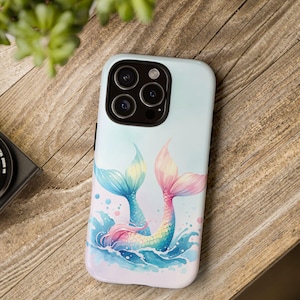 May include: A phone case with a colorful mermaid tail design. The tail is pink, blue, and green and is surrounded by blue water with white bubbles. The case is white with a light blue background.