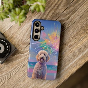 May include: A blue phone case featuring a golden doodle dog with a purple collar, set against a backdrop of a beach and colorful fireworks. The case has a camera module with three lenses.
