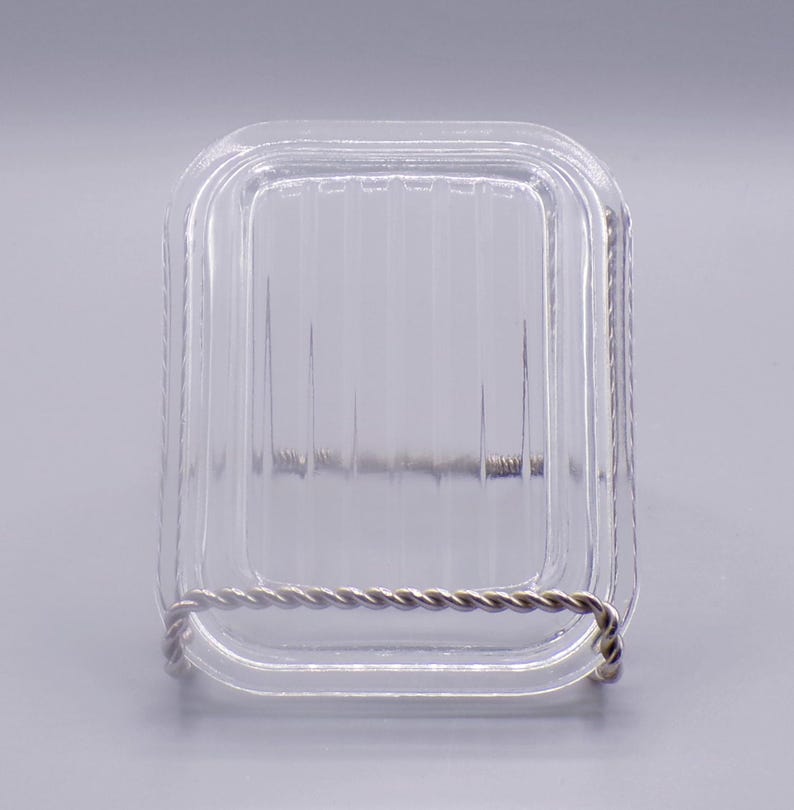 May include: A clear glass square dish with a silver wire rim. The dish has a ribbed pattern on the bottom.