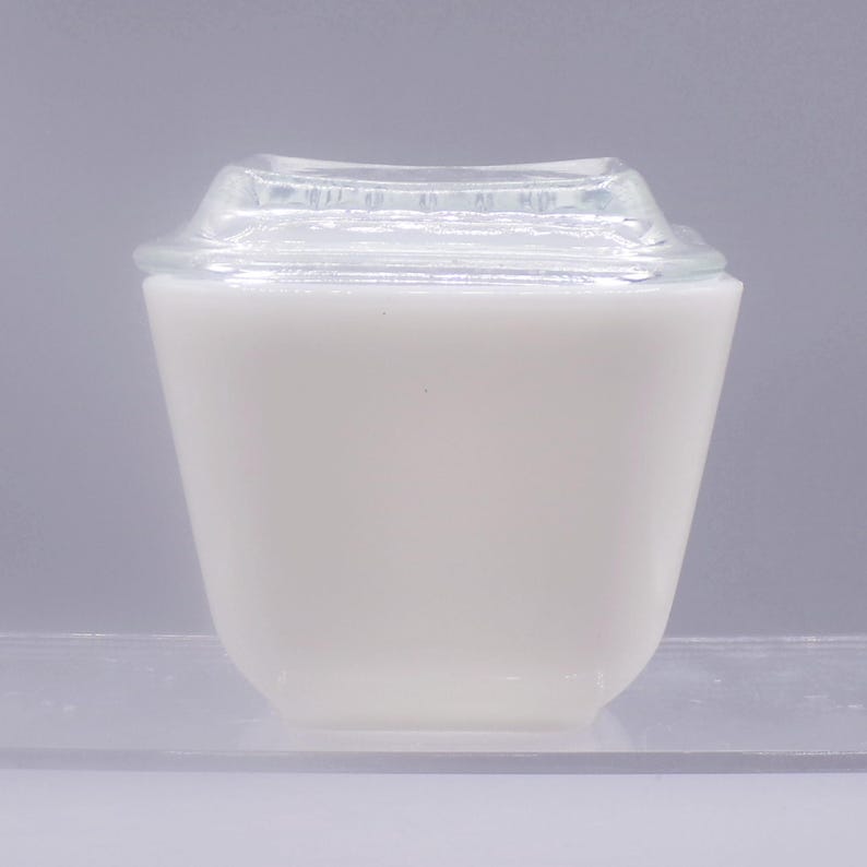 May include: White glass storage container with a clear glass lid. The container has a square shape with rounded corners.