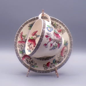 May include: A vintage teacup and saucer set with a floral pattern in shades of pink, green, and blue. The pattern features a tree with branches and leaves, and the border is a repeating geometric design.