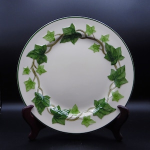 May include: A white ceramic dinner plate with a green ivy design around the rim.