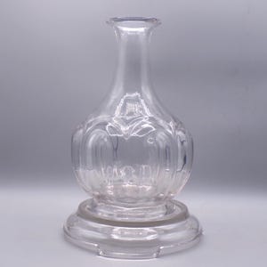 May include: A clear glass decanter with a round body and a flared neck. The decanter has a textured design and sits on a circular base.