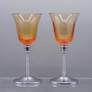 May include: Two amber colored stemmed glasses with a chrome base and a twisted chrome stem. The glasses have a ribbed design.