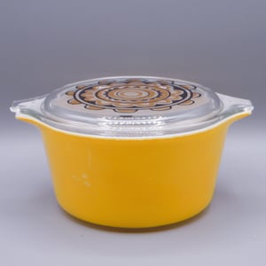 May include: Yellow ceramic casserole dish with a glass lid featuring a black and brown floral design.