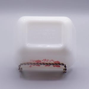 May include: White milk glass dish with a red floral design. The dish is on a metal stand. The bottom of the dish has the text "Fire King USA" printed on it.