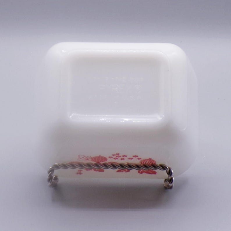 May include: White milk glass dish with a red floral design. The dish is on a metal stand. The bottom of the dish has the text "Fire King USA" printed on it.