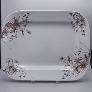 May include: A rectangular white serving platter with rounded corners. The platter is decorated with a brown floral pattern in the corners. The platter is supported by a clear plastic stand.