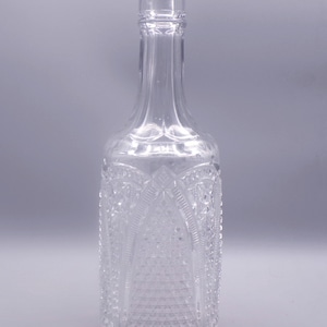 May include: A clear glass bottle with a textured surface. The bottle has a wide base and a narrow neck.
