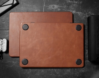 May include: Two brown leather laptop sleeves stacked on top of each other. The sleeves have black rubber feet on the bottom.