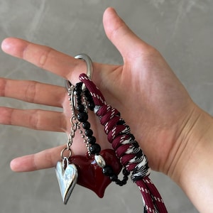Peut inclure: Un porte-cl&eacute;s avec un charm en forme de c&oelig;ur argent&eacute;, un pendentif en forme de c&oelig;ur rouge et des perles noires. Le porte-cl&eacute;s comprend &eacute;galement un cordon tress&eacute; bordeaux et noir et un grand anneau argent&eacute;.