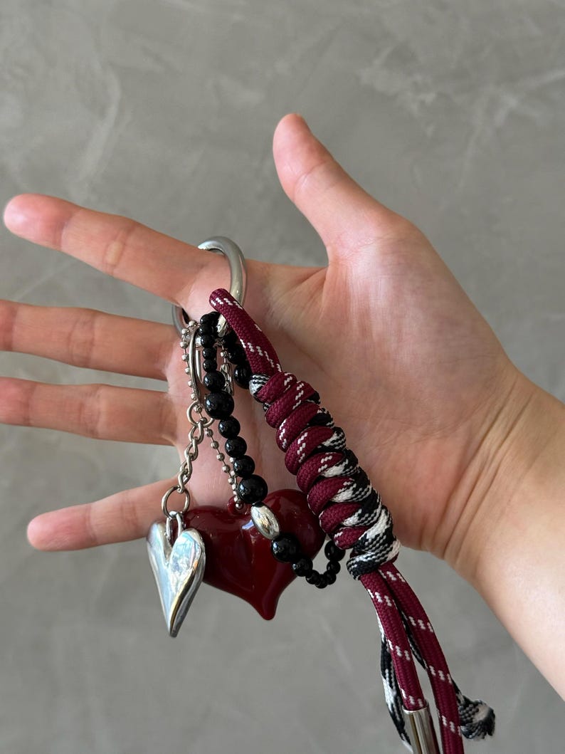 Peut inclure: Un porte-cl&eacute;s avec un charm en forme de c&oelig;ur argent&eacute;, un pendentif en forme de c&oelig;ur rouge et des perles noires. Le porte-cl&eacute;s comprend &eacute;galement un cordon tress&eacute; bordeaux et noir et un grand anneau argent&eacute;.
