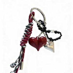 Peut inclure: Un porte-cl&eacute;s avec un charm en forme de c&oelig;ur bordeaux, un charm en forme de c&oelig;ur argent&eacute; et des perles noires. Il comprend un cordon tress&eacute; bordeaux, noir et blanc et un fermoir argent&eacute;.